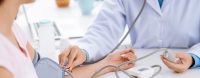 Symbolbild Arzt misst gerade Blutdruck bei einer Patientin fuer den Fuehrungskraefte-Checkup